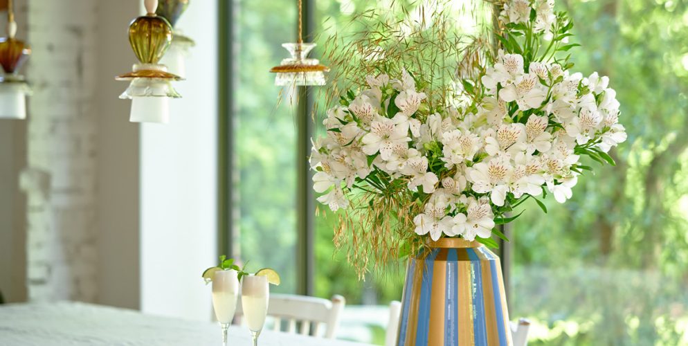 Witte Alstroemeria's in een kleurrijke vaas op een tafel in een lichte woonkamer.